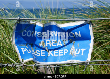 Blue conservation sign, battered and bent on a seaside wire fence. UK. Stock Photo