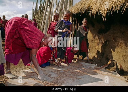 A MAASAI woman scrapes a cowhide surrounded by village children NGORONGORO CRATER TANZANIA Stock Photo