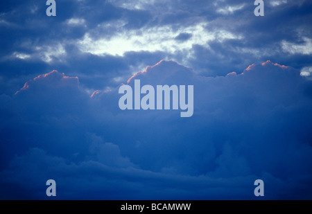 Majestic billowing storm clouds rimmed by a golden-red glowing sunset. Stock Photo