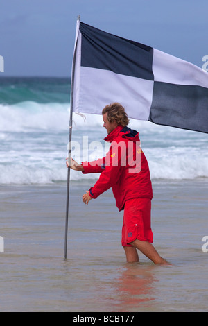 RNLI Lifeguard plants flag in waves off Porthmeor beach in summer sun St Ives Cornwall England UK United Kingdom GB Great Britai Stock Photo