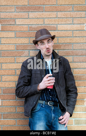 Cool guy leaning against brick wall with cup of coffee Stock Photo