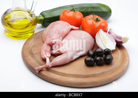 Raw rabbit legs with vegetables and olive oil on a wooden cutting board Stock Photo