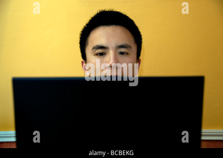Young Chinese Student in France, Portrait People Looking at Laptop Computer Screen working from home alone, man face Frontal, young person laptop Stock Photo