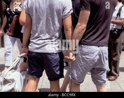New York City Two young gay men holding hands among a crowd  of people. Homosexuality and romance in USA Stock Photo