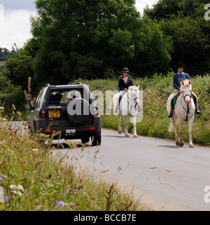 Horse riders pass a car on a country road in the Cotswolds Gloucestershire England UK Stock Photo