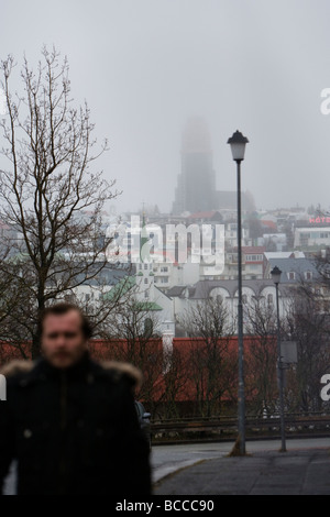 Man walking during a rainy foggy day Hallgrimskirkja church in the background Downtown Reykjavik Iceland Stock Photo