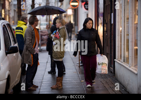 Man and woman talking on Laugavegur street, holding umbrella. woman walking by.  Laugavegur is Reykjavik s main shopping street Stock Photo