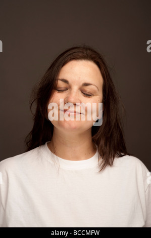 A thirty year old woman with long brown hair wearing white t shirt with her eyes closed smiling Stock Photo
