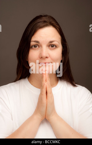 a thirty year old woman with long brown hair wearing white t shirt holding her hands together in prayer Stock Photo