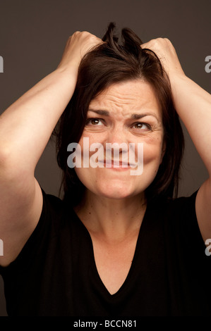 A thirty year old adult woman tearing at her long brown hair in anger and frustration Stock Photo