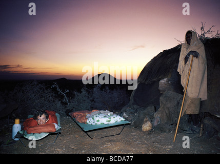 Camp beds Mark Jones and Rendille elder man outside Rendille hut on night of new moon Korr Northern Kenya East Africa Stock Photo