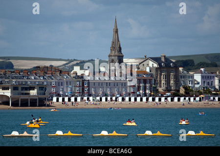 View of pedaloes in front of the sandy beach and the spire of St.Jonh's Church at Weymouth Dorset Stock Photo