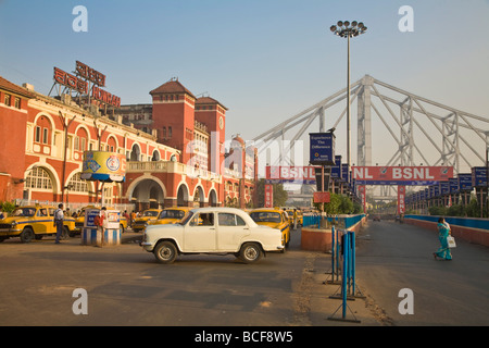 India, West Bengal, Kolkata, Calcutta, Yellow ambassador taxis outside Howrah train station with Howrah bridge in background Stock Photo