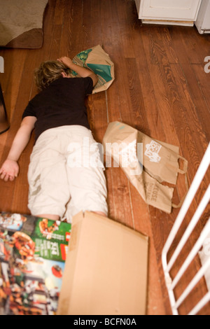 ten year old boy laying down on the floor at home, tired after playing all day, surrounded by cardboard boxes Stock Photo