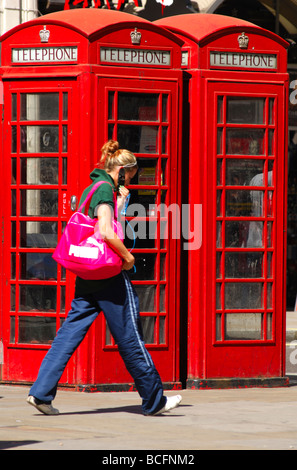 Young woman with a mobilie phone passing by tradional red telephone boxes in London, United Kingdom Stock Photo