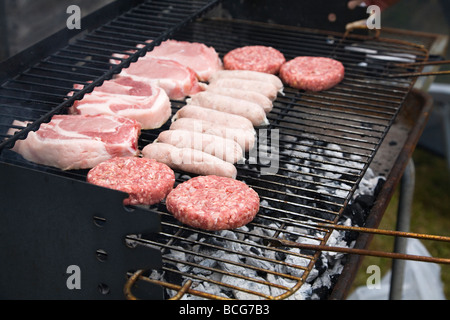 Fresh raw meat,  burgers, sausages and pork chops, cooking on a barbecue grill. England, UK. Stock Photo
