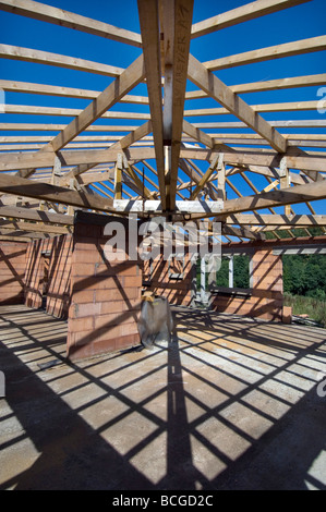 Shadows of roof trusses and wooden beams criss cross the floor and walls of a house under construction Stock Photo
