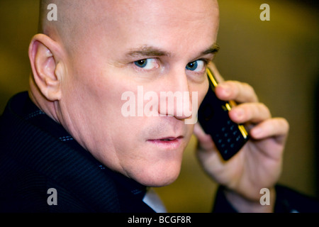Bald man in his late 40's wearing a dark suit speaking on a cell phone. Stock Photo