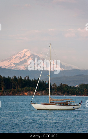 A sailboat anchors off Lummi Island, Washington. Snow capped Mt. Baker and the Lummi Indian Reservation dominate the background. Stock Photo