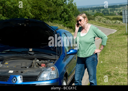 Lone woman with a broken down car calling for help on a mobile phone Stock Photo