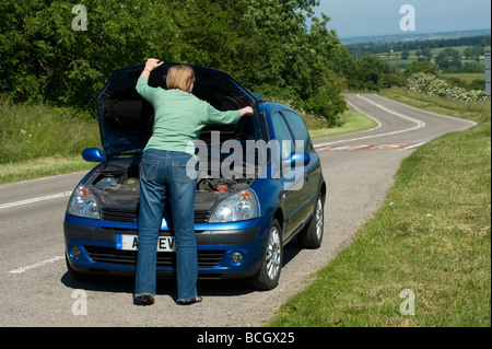 Lone woman lifting the bonnet of a broken down car at the side of the road Stock Photo