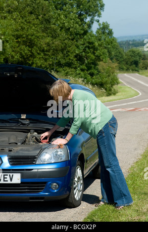 Lone woman looking under the bonnet of a broken down car at the side of the road Stock Photo