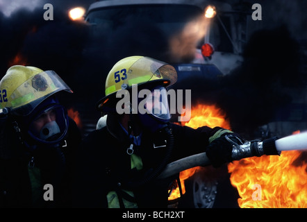 Two city firemen spray water from fire hose on burning city fire in Southern California. Stock Photo