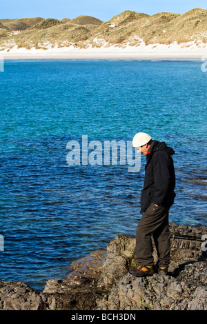 Man in outdoor gear standing on rocks at seaside at Balnakeil Bay, Durness, Scotland looking down at the sea Stock Photo