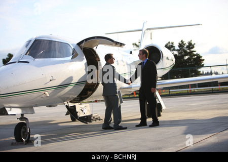 Businessmen shake hands by corporate jet Stock Photo