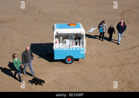 Holidaymakers walk past an ice cream seller and his van on the beach at Whitby in North Yorkshire. Stock Photo