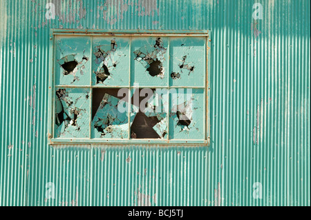 Green corrugated metal wall with broken glass windows Stock Photo