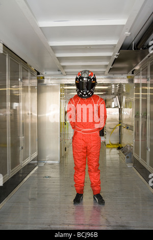 Race car driver wearing helmet and red jump suit standing inside metal transport vehicle Stock Photo