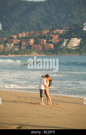 Ixtapa Mexico Couple kissing while standing on beach with ocean and hotels condominiums in background Stock Photo