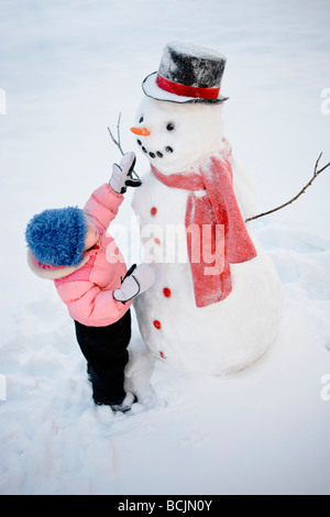 Young girl decorates a snowman with red scarf and black top hat, Alaska Stock Photo