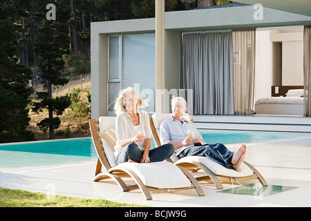 Middle aged couple relaxing on deck chairs by the pool Stock Photo