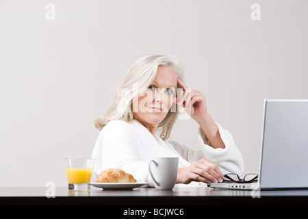 Middle aged woman using laptop at breakfast time Stock Photo