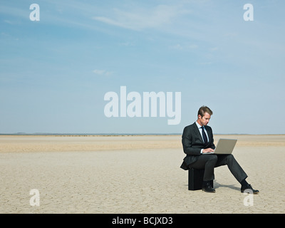 Businessman sitting on a briefcase in the desert Stock Photo