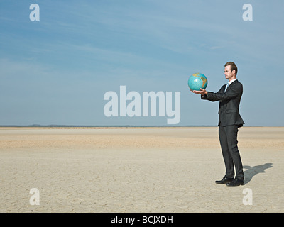 Businessman holding a globe in desert Stock Photo