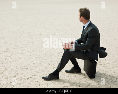 Businessman sitting on a briefcase in the desert Stock Photo