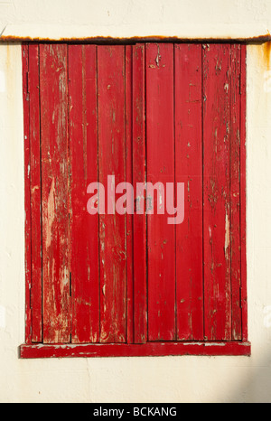 Old sea battered and weathered red window shutters closed and in need of repair and painting, Kingsand, Cornwall, UK Stock Photo