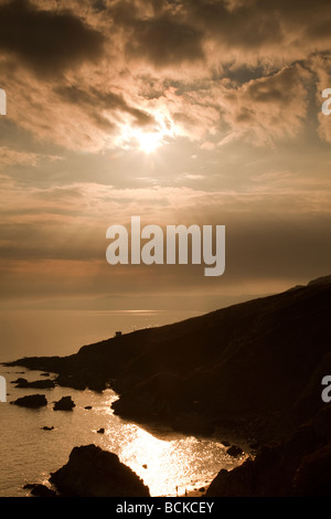 Setting sun over RNLI lifeguard cabin at base of Cornish cliffs, Whitsand Bay, Cornwall, UK Stock Photo