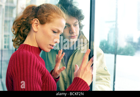 Young man and woman on either side of glass door Stock Photo