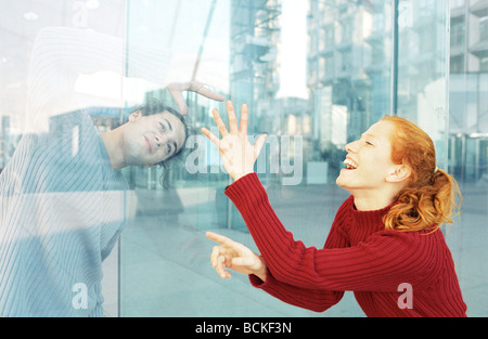 Young man and woman on either side of glass door, laughing Stock Photo