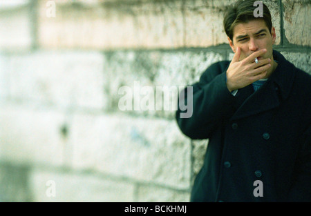 Man standing next to wall, smoking Stock Photo