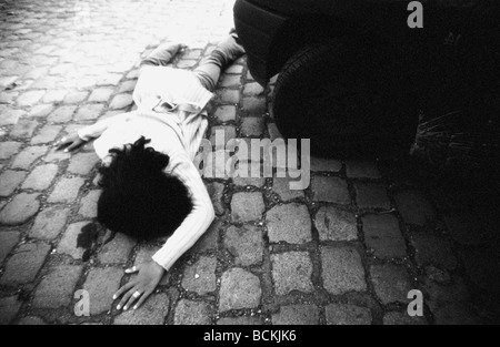 Woman lying face down on paving stones next to car, b&w Stock Photo