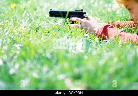 Child lying on grass pointing gun, surface level side view Stock Photo