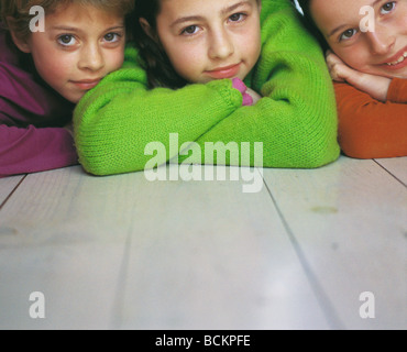 Three girls lying on stomachs on floor, looking at camera, front view Stock Photo