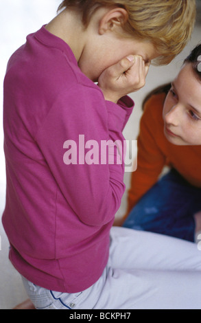 Two girls on floor, one kneeling and covering face with hands Stock Photo