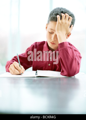 Boy writing at table with hand on forehead, front view Stock Photo