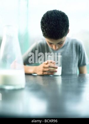 Boy sitting at table looking down into glass of milk, carafe of milk in foreground Stock Photo